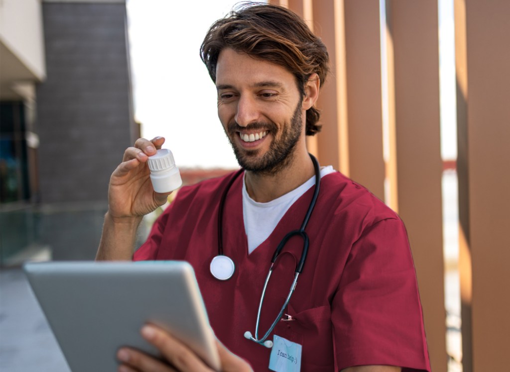 a male medical professional holding a tablet computer and a prescription bottle