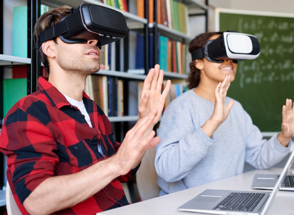 a group of people wearing virtual reality headsets while sitting at a table using laptops