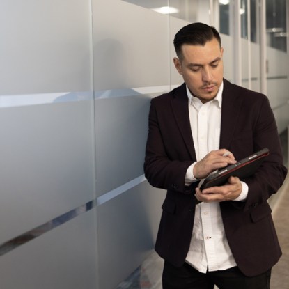 a businessman wearing a suit stands in a hallway working on a tablet computer