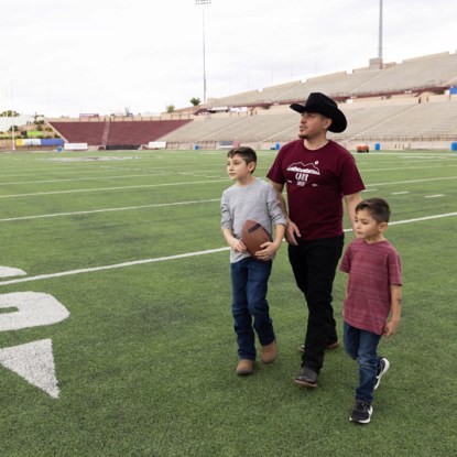 An Aggie dad and his two sons walk on NMSU's football field