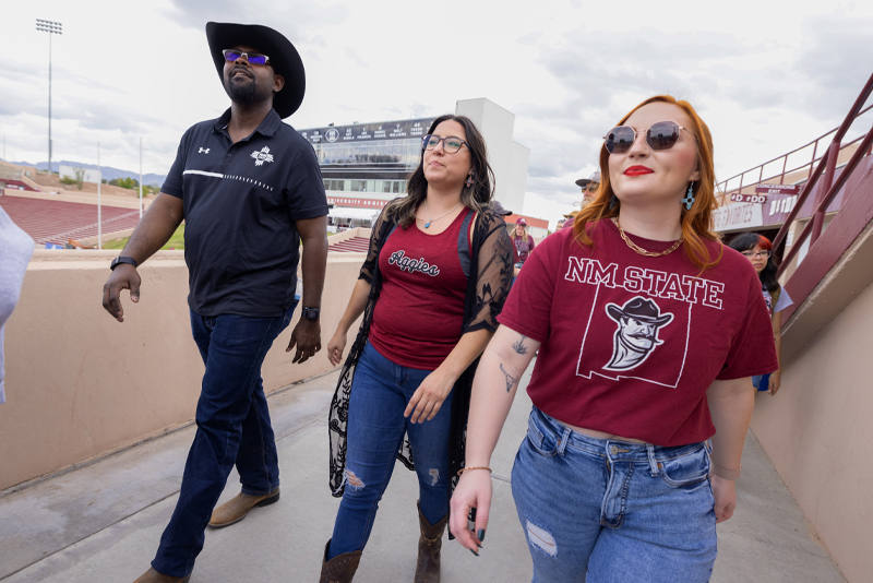 A group of NMSU students posing walks through the stadium.