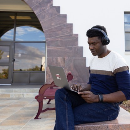 A young man wearing headphones studies online with his laptop.