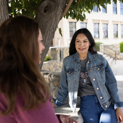 Two women chat under a tree on the beautiful NMSU campus.