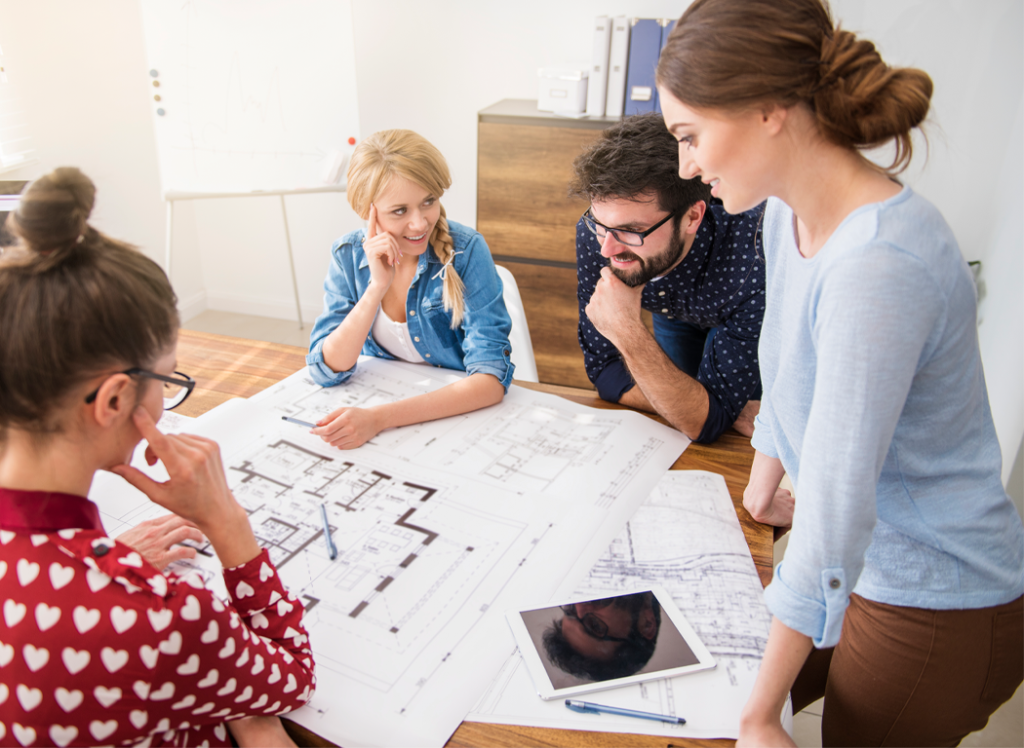 A group of coworkers sits around a conference table collaborating over a blueprint