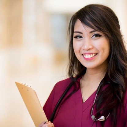 A smiling nurse wears crimson scrubs and a stethoscope