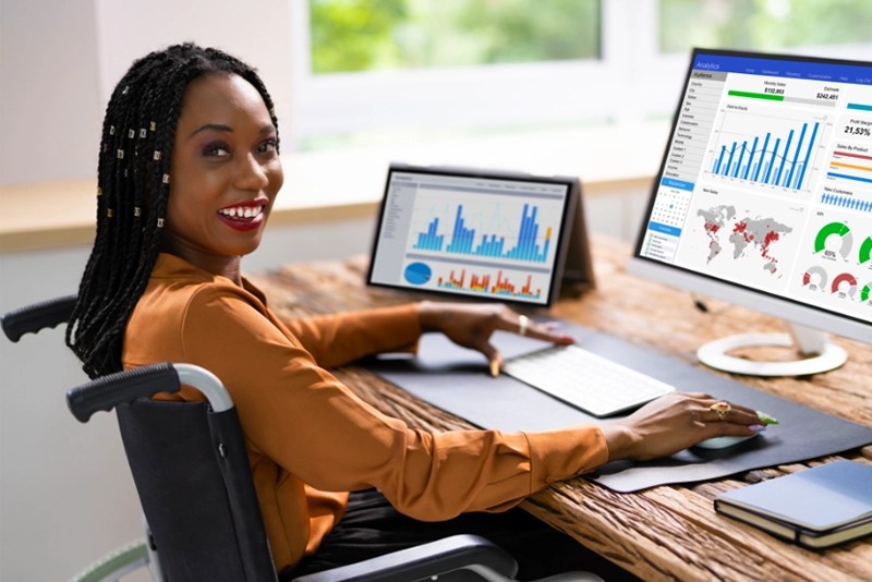 A woman using a wheelchair works on multiple screens on her desktop