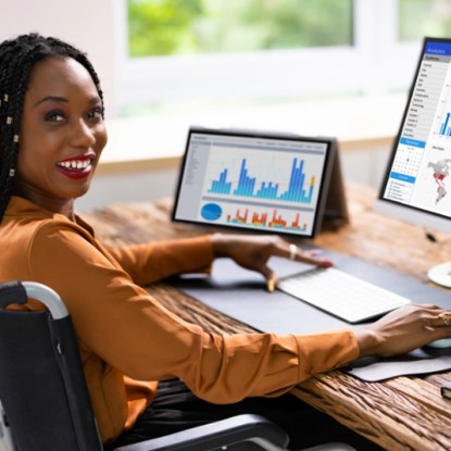 A woman using a wheelchair works on multiple screens on her desktop