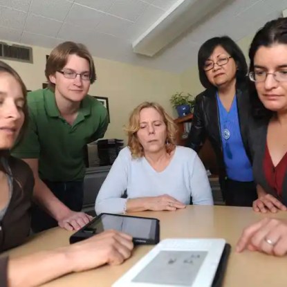 Five people looking closely at a tablet computer on a conference table — NMSU Global Campus