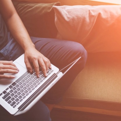 A person sits on a sofa while typing on a laptop