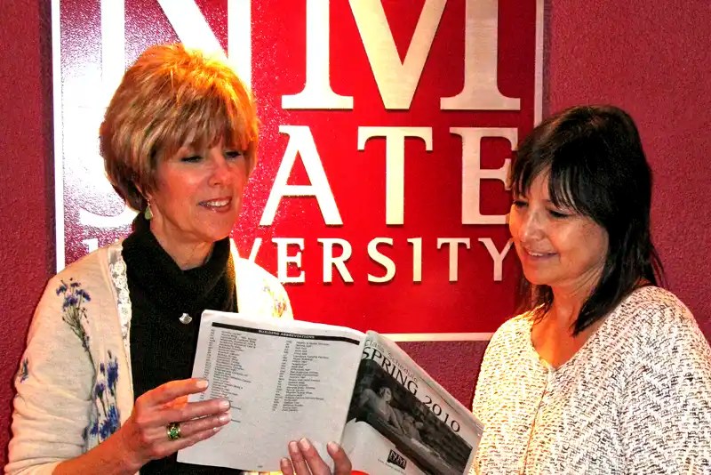 Two women stand in front of the NMSU logo reviewing a class schedule — NMSU Global Campus