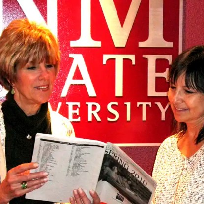 Two women stand in front of the NMSU logo reviewing a class schedule — NMSU Global Campus