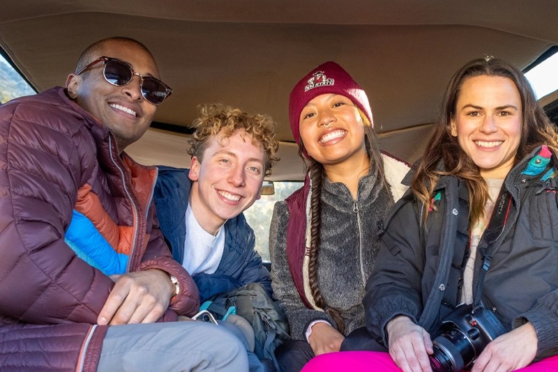 a smiling group of college students sitting in a car