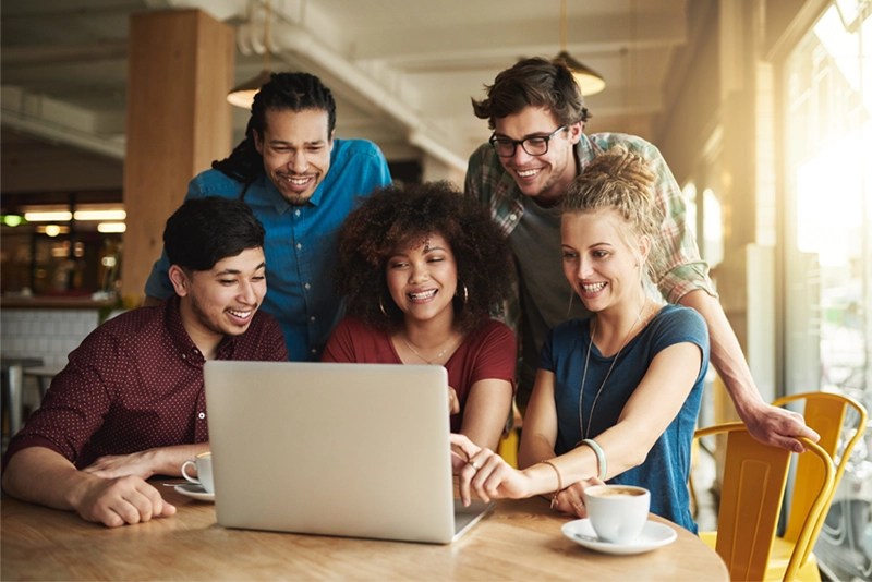 a group of excited young women and men looking at a laptop