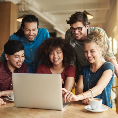 a group of excited young women and men looking at a laptop