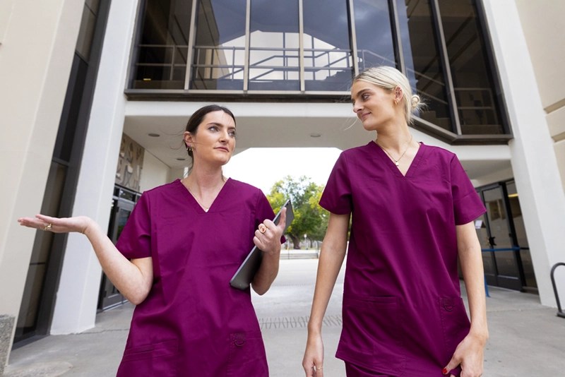 Two nurses wearing scrubs walk and talk outdoors