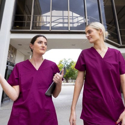 Two nurses wearing scrubs walk and talk outdoors