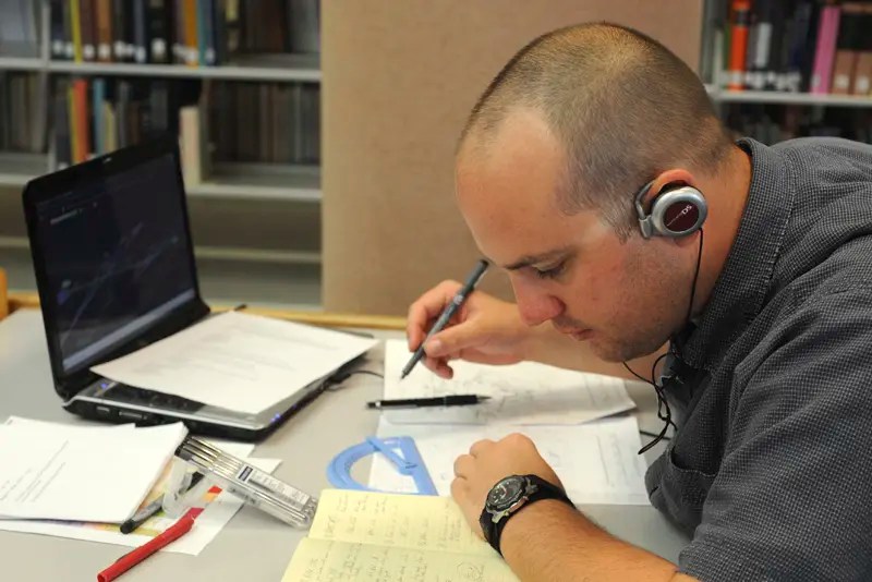 A man does online homework on his laptop in a library — NMSU Global Campus 