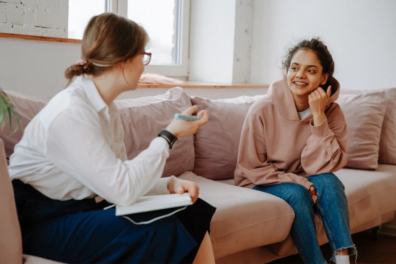 two women sitting and talking on a couch