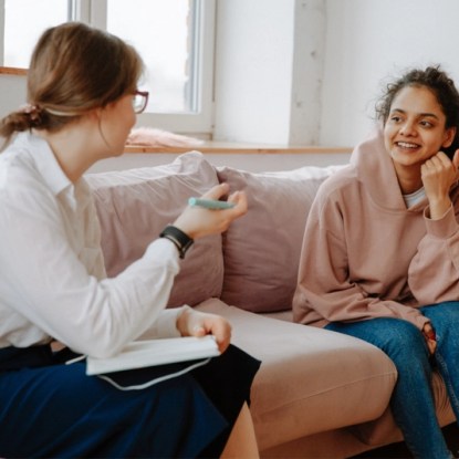 two women sitting and talking on a couch