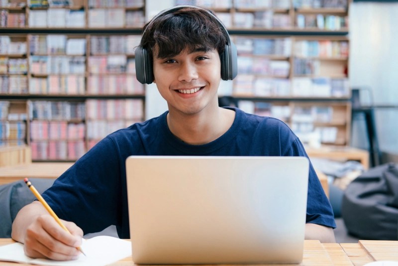 a boy wearing headphones and sitting at a desk with a laptop