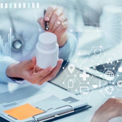 close-up of hands holding a bottle of medicine beside a clipboard and a laptop computer