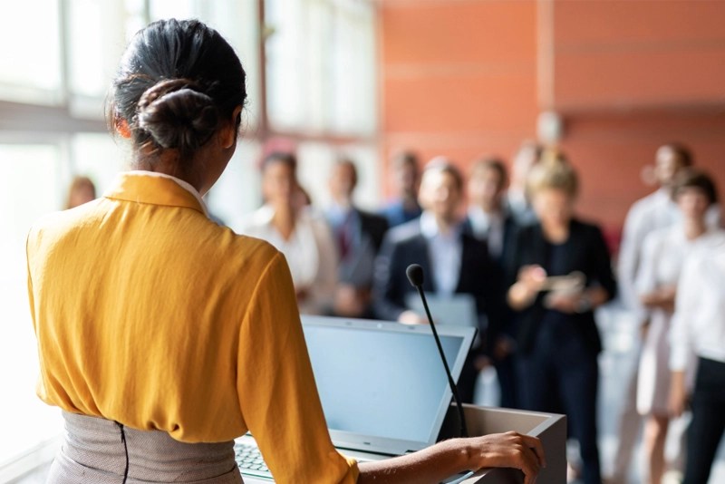 a woman answers reporters' questions from a podium