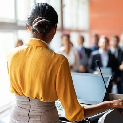 a woman answers reporters' questions from a podium