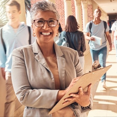 A school principal holds a clipboard as students walk by