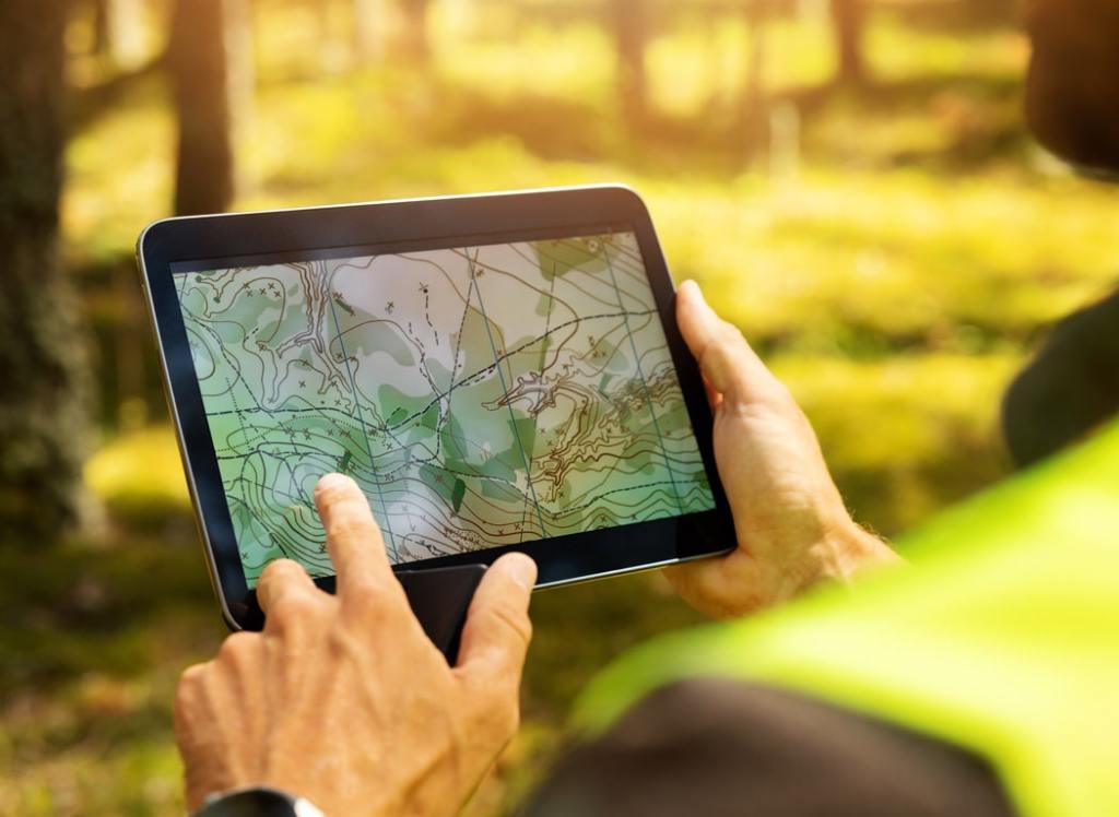 Person using a tablet to view a topographic map in a forested area