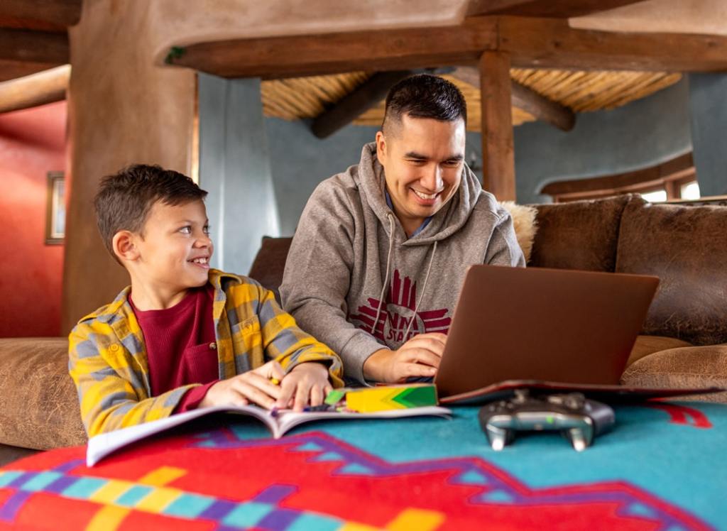 Smiling father and son working together at a colorful table with books and a laptop