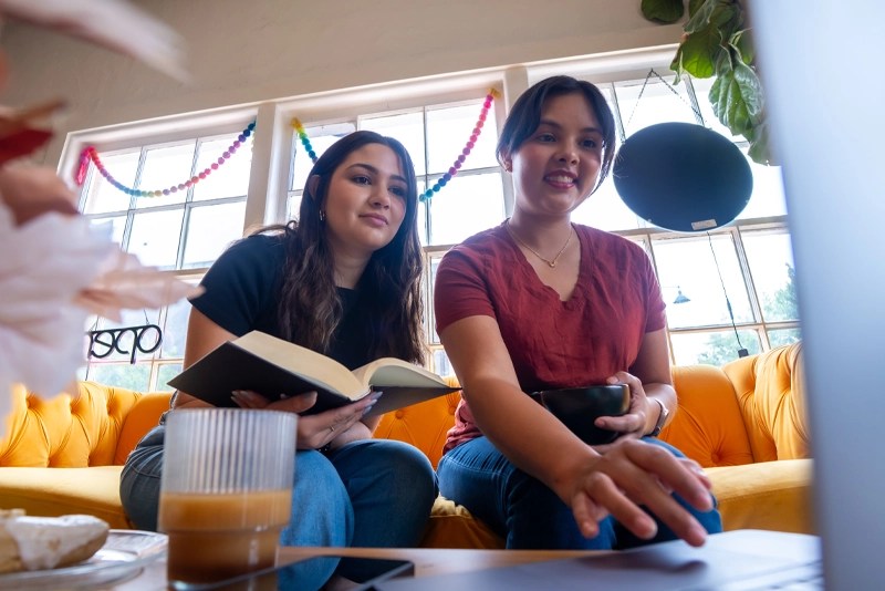 Two students study together on a bright yellow couch, using a laptop and notebook—representing online business degree students at NMSU Global Campus in 2025.