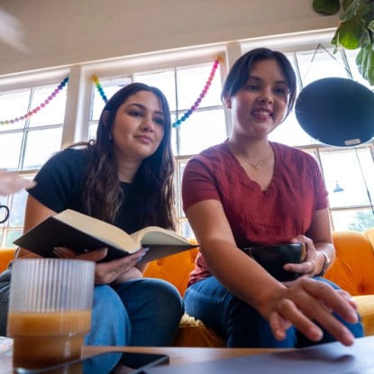 Two students study together on a bright yellow couch, using a laptop and notebook—representing online business degree students at NMSU Global Campus in 2025.