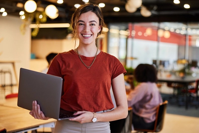 Woman holds a laptop in a modern office — Workforce development partnerships and online training with NMSU Global Campus