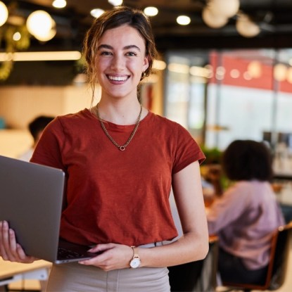 Woman holds a laptop in a modern office — Workforce development partnerships and online training with NMSU Global Campus