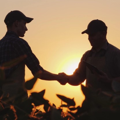 Farmers shaking hands in a field at sunset, representing the online master's in agribusiness at NMSU Global Campus
