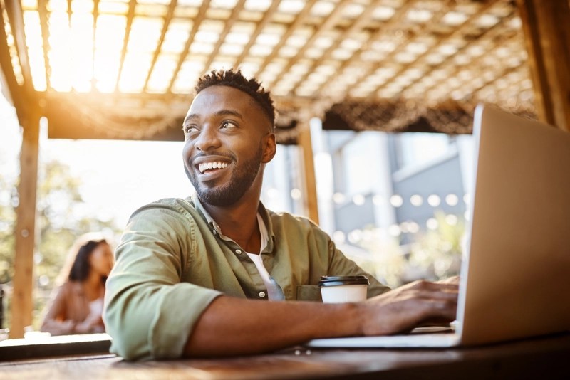 An adult learner takes online courses on his laptop from an outdoor coffee shop — NMSU Global Campus