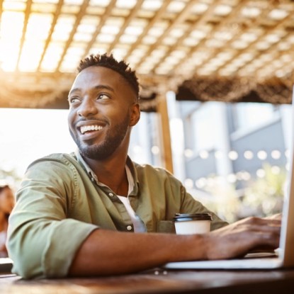 An adult learner takes online courses on his laptop from an outdoor coffee shop — NMSU Global Campus