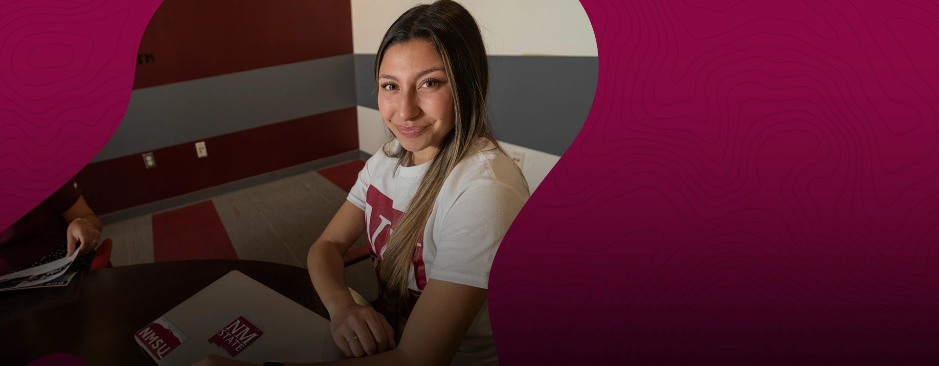 A college student in an NMSU t-shirt holds her laptop — New Mexico State University Global Campus
