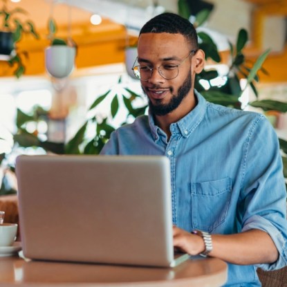 A man in denim shirt types on his laptop in a cafe — NMSU Global Campus microlearning vs traditional college degrees online