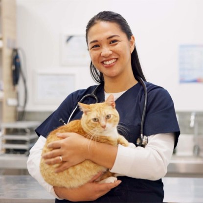 A smiling veterinary technician poses with an orange tabby cat