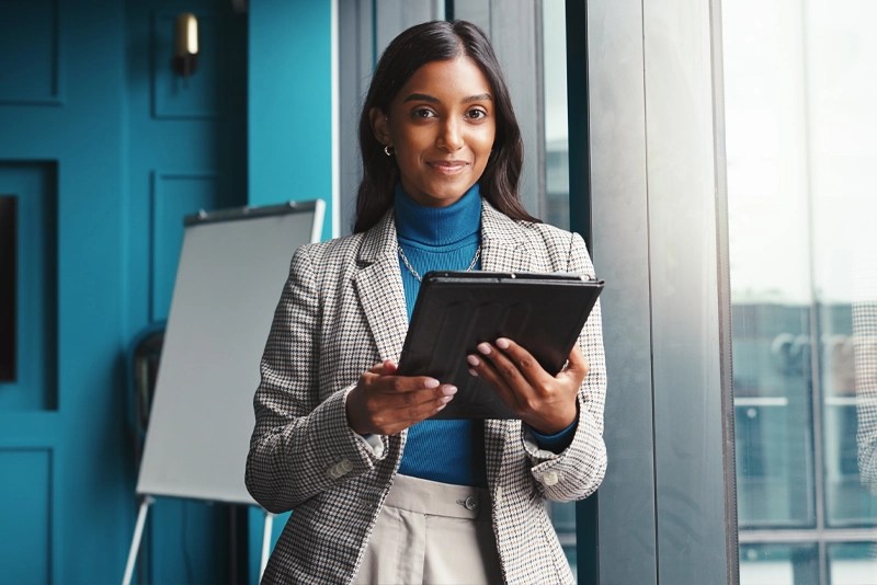 A smiling woman in business attire holds a tablet computer