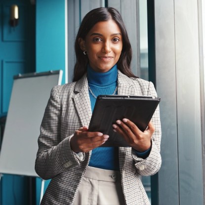 A smiling woman in business attire holds a tablet computer