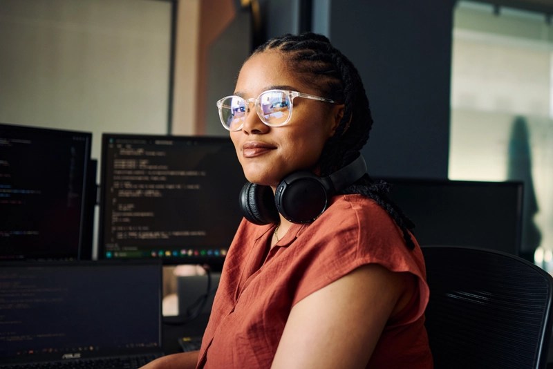 A woman wearing glasses poses by computer terminals