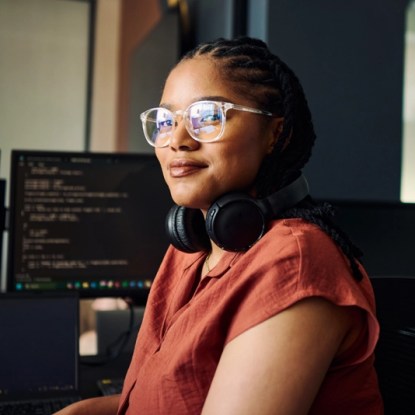 A woman wearing glasses poses by computer terminals