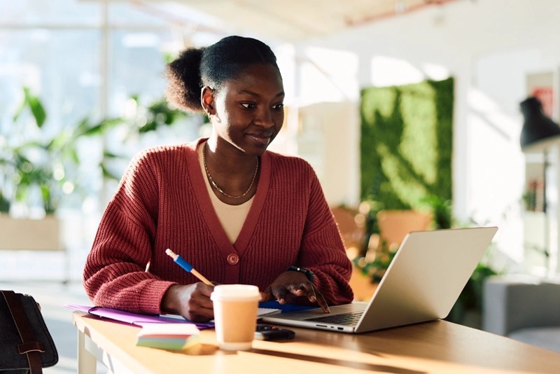 A young woman takes notes while watching an online course on her laptop — NMSU Global Campus