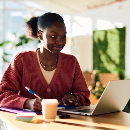 A young woman takes notes while watching an online course on her laptop — NMSU Global Campus