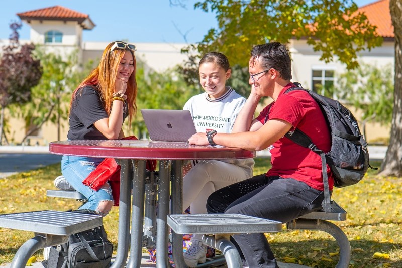 Three New Mexico State University students sit outdoors at a picnic table