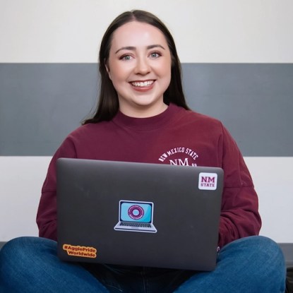 A smiling NMSU Global Campus student sits crosslegged with her laptop
