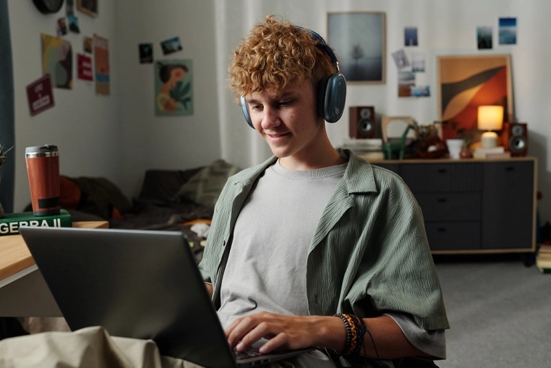 A high school student wearing headphones and working on a laptop computer