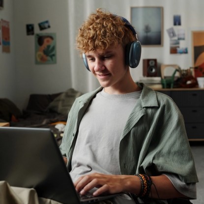 A high school student wearing headphones and working on a laptop computer